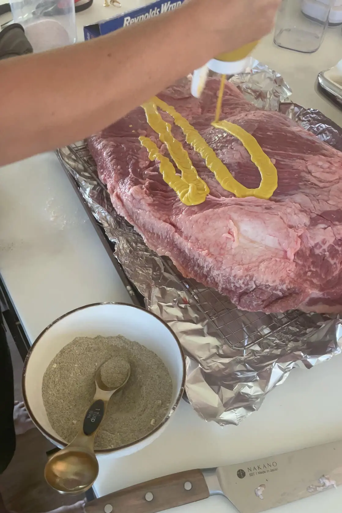 Covering a brisket with mustard before smoking.